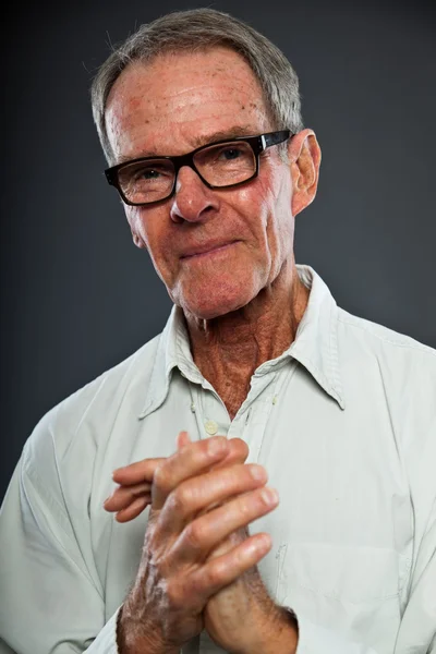Uttrycksfulla bra söker äldre man med glasögon mot grå vägg. händerna bedjande. andliga och karakteristiska. välklädd. Studio skott. — Stockfoto