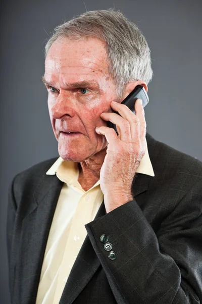Hombre mayor expresivo y bien parecido en traje oscuro contra pared gris. Llamando con el teléfono celular. Gracioso y característico. Bien vestido. Captura de estudio . —  Fotos de Stock