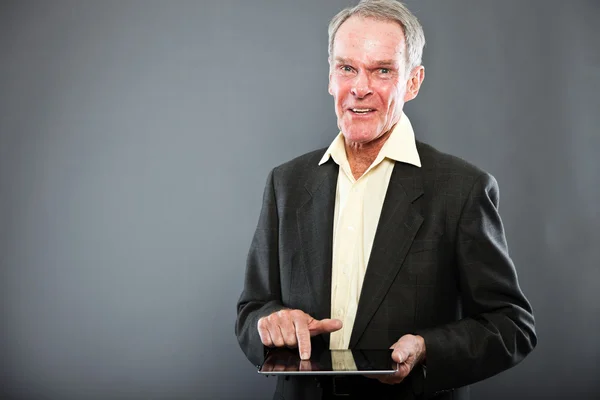 Uttrycksfulla snygg äldre man i mörk kostym mot grå vägg. med hjälp av Tablet PC. rolig och karakteristiska. välklädd. Studio skott. — Stockfoto