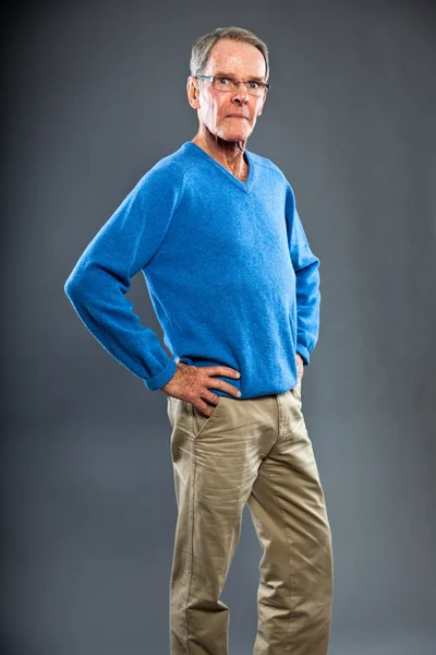 Hombre mayor expresivo y bien parecido contra la pared gris. Gracioso y característico. Bien vestido. Jersey azul. Captura de estudio . —  Fotos de Stock