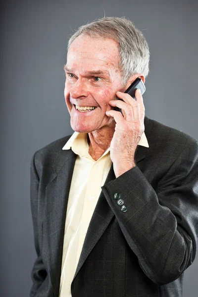 Виразно добре виглядає старший чоловік у темному костюмі проти сірої стіни. Дзвінок з мобільним телефоном. Смішно і характерно. Добре одягнений. Студійний знімок . — стокове фото