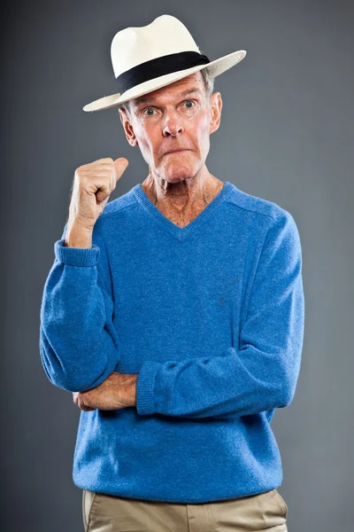 Ausdrucksstarker gut aussehender älterer Herr gegen graue Wand. mit Hut. Witzig und charakteristisch. Gut angezogen. blauer Pullover. Studioaufnahme. — Stockfoto