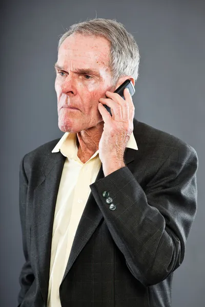 Udtryksfuld flot senior mand i mørkt jakkesæt mod grå væg. Ringer med mobiltelefon. Sjovt og karakteristisk. Godt klædt på. Studieoptagelse . - Stock-foto