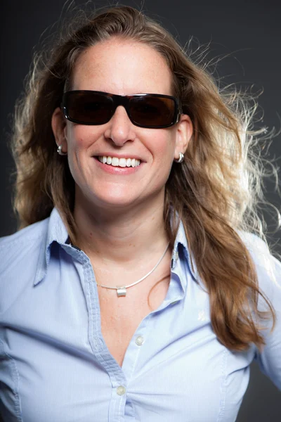 Mujer bonita pelo largo y rubio con gafas de sol y camisa azul claro. Aislado sobre fondo gris. Captura de estudio . —  Fotos de Stock