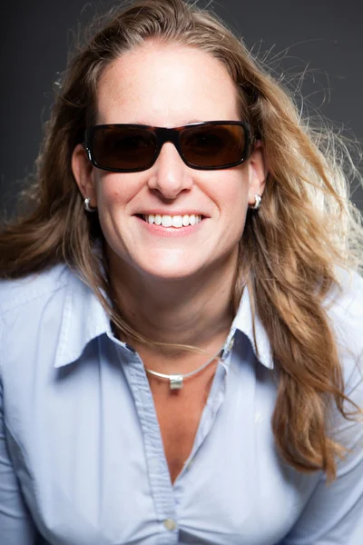 Mujer bonita pelo largo y rubio con gafas de sol y camisa azul claro. Aislado sobre fondo gris. Captura de estudio . —  Fotos de Stock