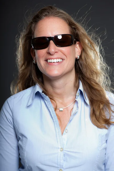 Hübsche Frau mit langen blonden Haaren, Sonnenbrille und hellblauem Hemd. isoliert auf grauem Hintergrund. Studioaufnahme. — Stockfoto