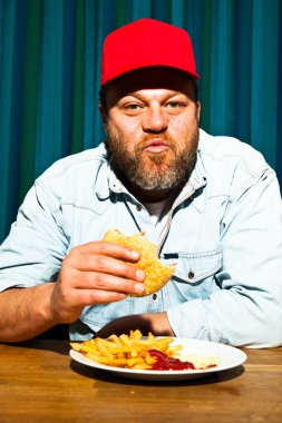 fast food yemek yeme sakallı adam. hamburger ve patates kızartması tadını çıkarıyor. kırmızı bere ile kamyon şoförü.