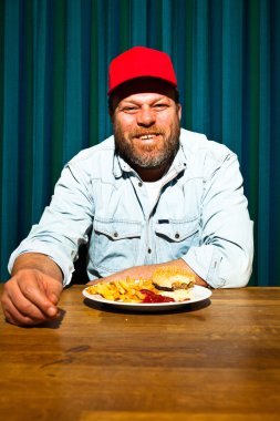 fast food yemek yeme sakallı adam. hamburger ve patates kızartması tadını çıkarıyor. kırmızı bere ile kamyon şoförü.