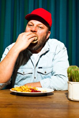 fast food yemek yeme sakallı adam. hamburger ve patates kızartması tadını çıkarıyor. kırmızı bere ile kamyon şoförü.