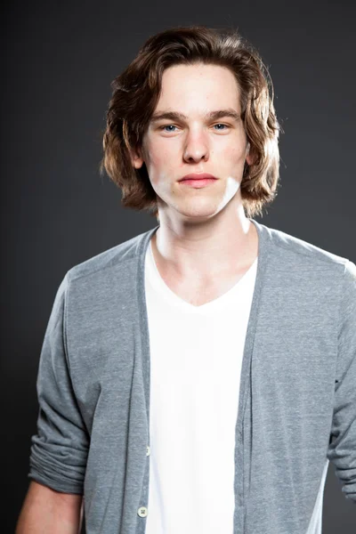 Handsome young man with brown long hair isolated on grey background. Fashion studio shot. — Stock Photo, Image