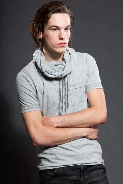 Beau jeune homme aux cheveux longs bruns portant une chemise grise isolée sur fond gris. Studio de mode tourné. Visage expressif . — Photo
