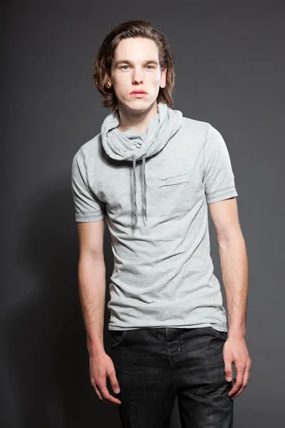 Schöner junger Mann mit braunen langen Haaren, graues Hemd auf grauem Hintergrund. Modestudio gedreht. Gesichtsausdruck. — Stockfoto