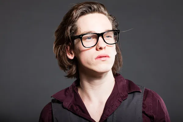 Handsome young man with brown long hair isolated on grey background. Wearing black retro glasses. Fashion studio shot. Expressive face. — Stock Photo, Image