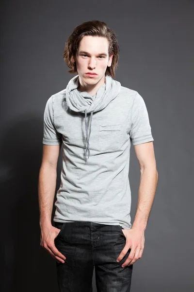 Stilig ung man med brunt långt hår iklädd grå skjorta isolerad på grå bakgrund. mode studio skott. uttrycksfulla ansikte. — Stockfoto