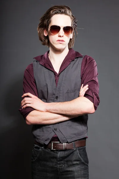 Schöner junger Mann mit braunen langen Haaren auf grauem Hintergrund. mit Sonnenbrille. Modestudio gedreht. Gesichtsausdruck. — Stockfoto