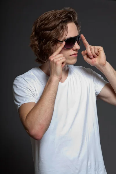 Stilig ung man med brunt långt hår och solglasögon isolerad på grå bakgrund. mode studio skott. — Stockfoto