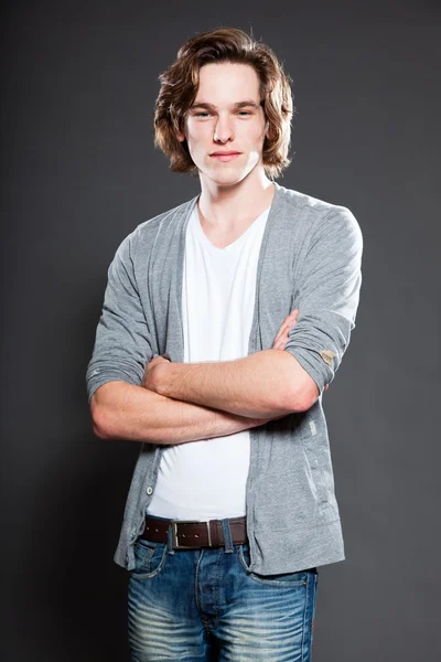 Schöner junger Mann mit braunen langen Haaren auf grauem Hintergrund. Modestudio erschossen. — Stockfoto