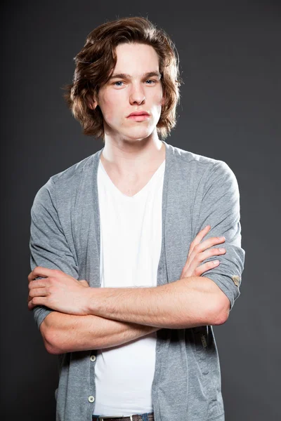 Schöner junger Mann mit braunen langen Haaren auf grauem Hintergrund. Modestudio erschossen. — Stockfoto