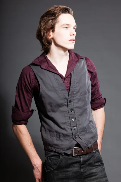 Schöner junger Mann mit braunen langen Haaren auf grauem Hintergrund. Modestudio gedreht. Gesichtsausdruck. — Stockfoto