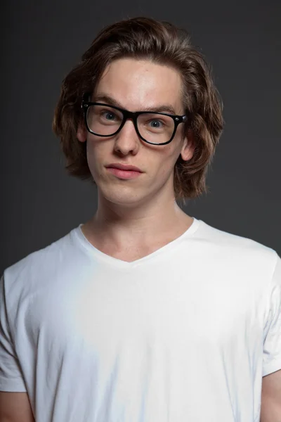 Schöner junger Mann mit braunen langen Haaren und Retro-Brille auf grauem Hintergrund. Modestudio gedreht. Gesichtsausdruck. — Stockfoto