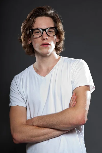 Beau jeune homme aux cheveux longs bruns et aux lunettes rétro isolées sur fond gris. Studio de mode tourné . — Photo