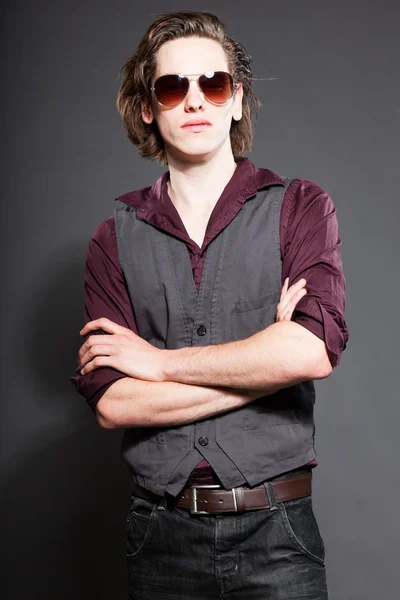 Handsome young man with brown long hair isolated on grey background. Wearing sunglasses. Fashion studio shot. Expressive face. — Stock Photo, Image