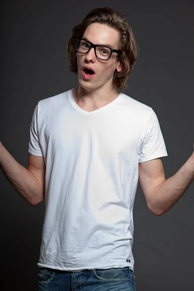 Handsome young man with brown long hair and retro glasses isolated on grey background. Fashion studio shot. Expressive face. — Stock Photo, Image