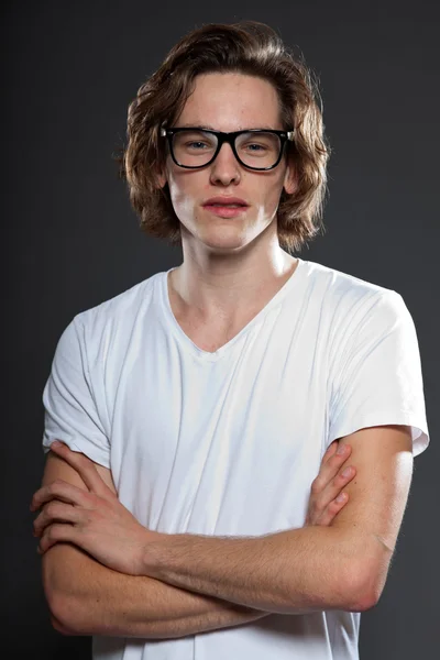 Όμορφος νεαρός άνδρας με καστανά μακριά μαλλιά και ρετρό γυαλιά που απομονώνονται σε γκρι φόντο. στούντιο μόδας πυροβόλησε. — Φωτογραφία Αρχείου