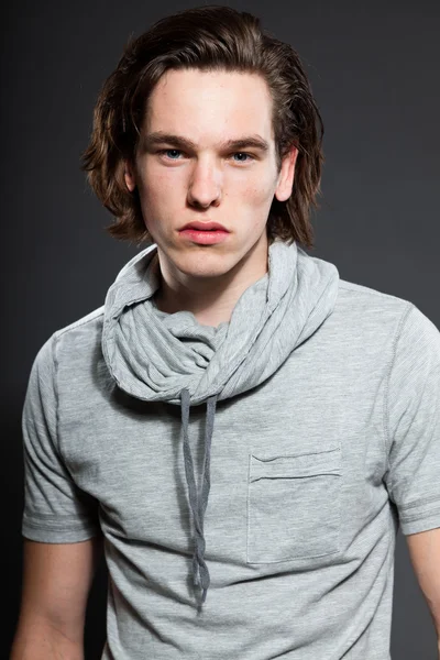 Handsome young man with brown long hair wearing grey shirt isolated on grey background. Fashion studio shot. Expressive face. — Stock Photo, Image