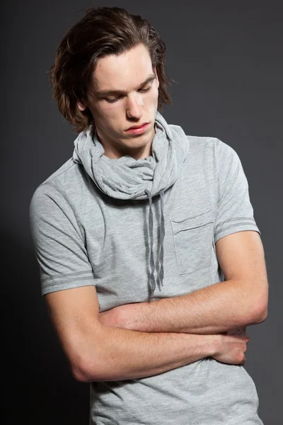 Handsome young man with brown long hair wearing grey shirt isolated on grey background. Fashion studio shot. Expressive face. — Stock Photo, Image