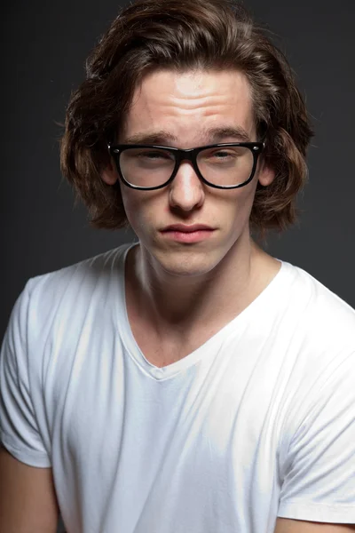 Όμορφος νεαρός άνδρας με καστανά μακριά μαλλιά και ρετρό γυαλιά που απομονώνονται σε γκρι φόντο. στούντιο μόδας πυροβόλησε. εκφραστικό πρόσωπο. — Φωτογραφία Αρχείου