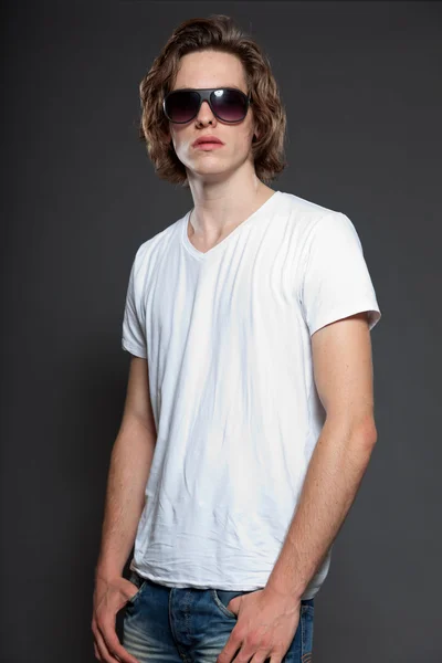 Bonito jovem com cabelos longos castanhos e óculos de sol isolados em fundo cinza. Estúdio de moda tiro . — Fotografia de Stock