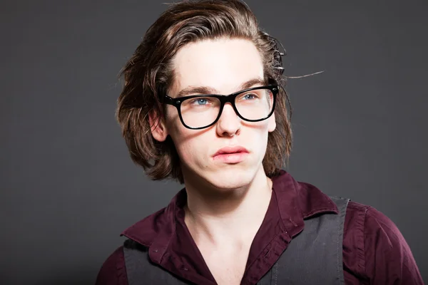 Handsome young man with brown long hair isolated on grey background. Wearing black retro glasses. Fashion studio shot. Expressive face. — Stock Photo, Image