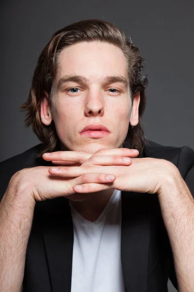 Schöner junger Mann mit braunen langen Haaren und weißem Hemd und blauer Jacke auf grauem Hintergrund. Modestudio gedreht. Gesichtsausdruck. — Stockfoto