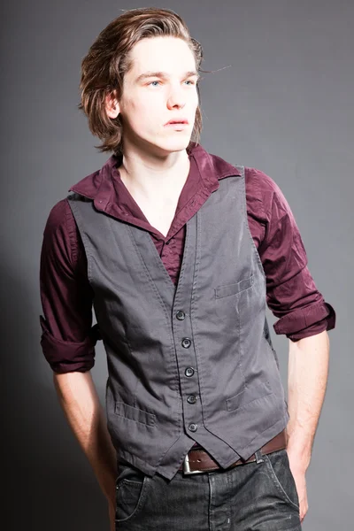 Schöner junger Mann mit braunen langen Haaren auf grauem Hintergrund. Modestudio gedreht. Gesichtsausdruck. — Stockfoto