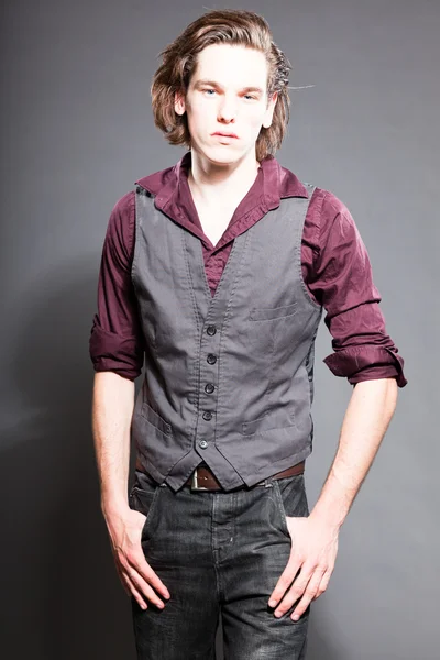Bel giovanotto con i capelli lunghi marroni isolati su sfondo grigio. Scatto dello studio di moda. Viso espressivo . — Foto Stock