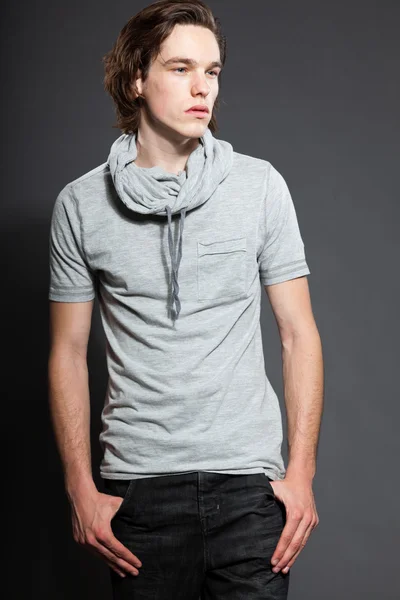 Bonito jovem com cabelo longo marrom vestindo camisa cinza isolado em fundo cinza. Estúdio de moda. Cara expressiva . — Fotografia de Stock