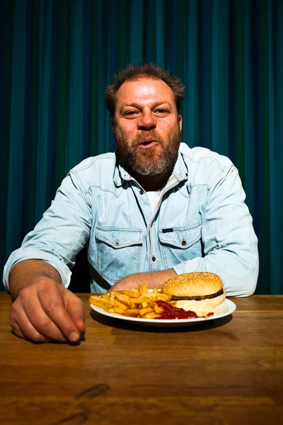 Hombre con barba comiendo comida rápida. Disfrutando de papas fritas y una hamburguesa . —  Fotos de Stock