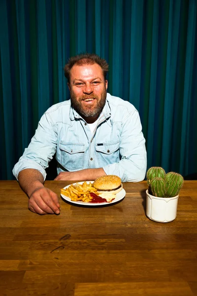 Man met baard eten van fast-food maaltijd. genieten van Franse frietjes en een hamburger. — Stockfoto
