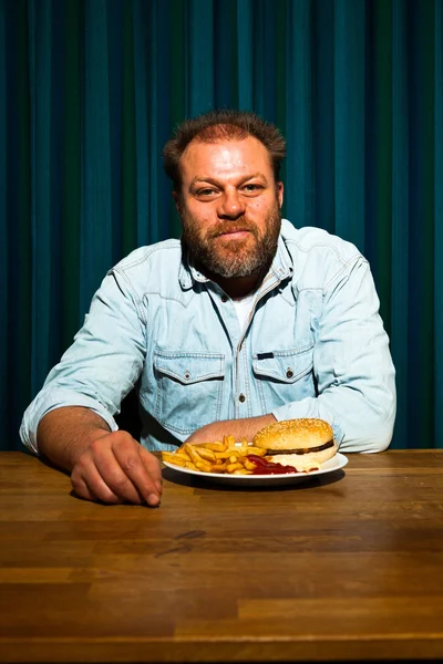 Férfi szakállal eszik gyorséttermi étkezés. élvezi a sült krumpli és egy hamburger. — Stock Fotó