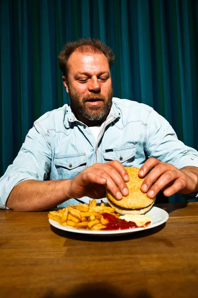 Mannen med skägget äter snabbmat måltid. njuter av pommes frites och en hamburgare. — Stockfoto
