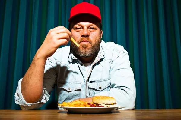 패스트 푸드 식사 수염을 가진 남자입니다. 감자 튀김과 햄버거를 즐기는. 빨간 모자와 트럭. — 스톡 사진