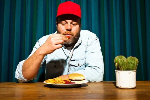 Чоловік з бородою їсть фаст-фуд. Насолоджуйтесь картоплею фрі та гамбургером. Трейлер з червоною шапочкою . — стокове фото