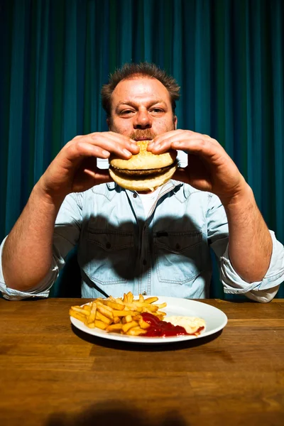 Mann mit Bart isst Fast-Food-Essen. Pommes und einen Hamburger genießen. — Stockfoto