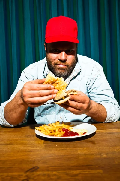 Homme à la barbe mangeant un repas de restauration rapide. Savourer des frites et un hamburger. Camionnette avec capuchon rouge . — Photo