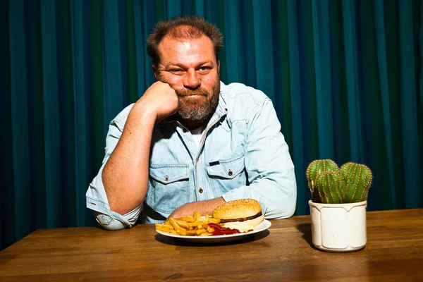 吃快餐餐大胡子的男人。享受法式炸薯条和汉堡. — 图库照片