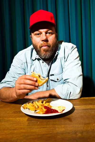 Чоловік з бородою їсть фаст-фуд. Насолоджуйтесь картоплею фрі та гамбургером. Трейлер з червоною шапочкою . — стокове фото