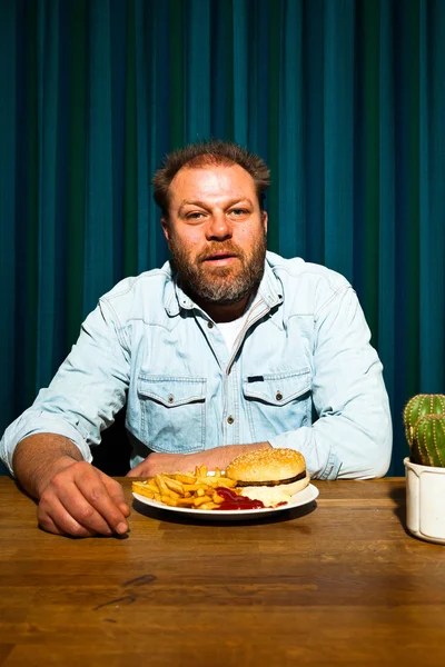 Férfi szakállal eszik gyorséttermi étkezés. élvezi a sült krumpli és egy hamburger. — Stock Fotó