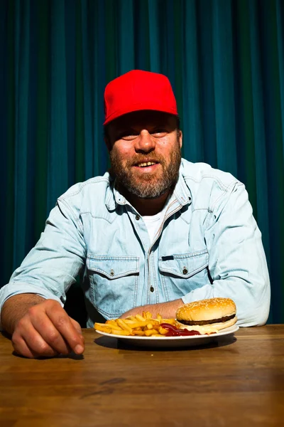 패스트 푸드 식사 수염을 가진 남자입니다. 감자 튀김과 햄버거를 즐기는. 빨간 모자와 트럭. — 스톡 사진