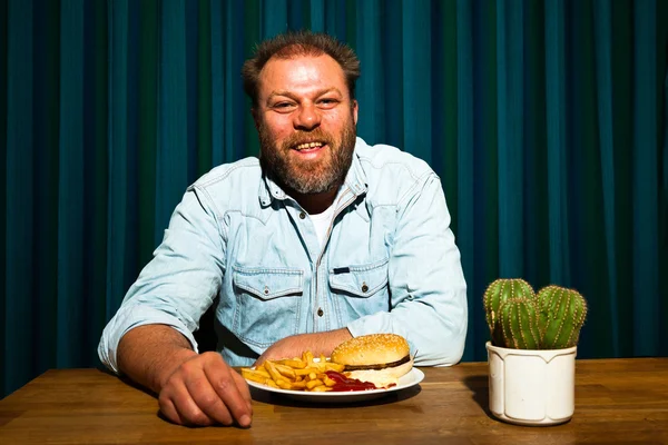Muž s plnovousem, fast food jídlo. francouzské hranolky a hamburger. — Stock fotografie